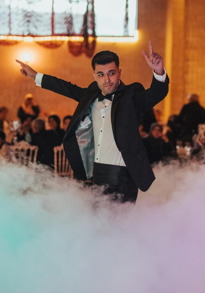 Man in tuxedo dancing through mist at a lively wedding celebration.